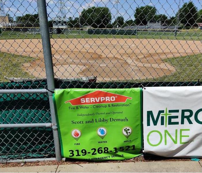 Diamond Baseball Field in front of a green fence with a bright green SERVPRO sign on it.