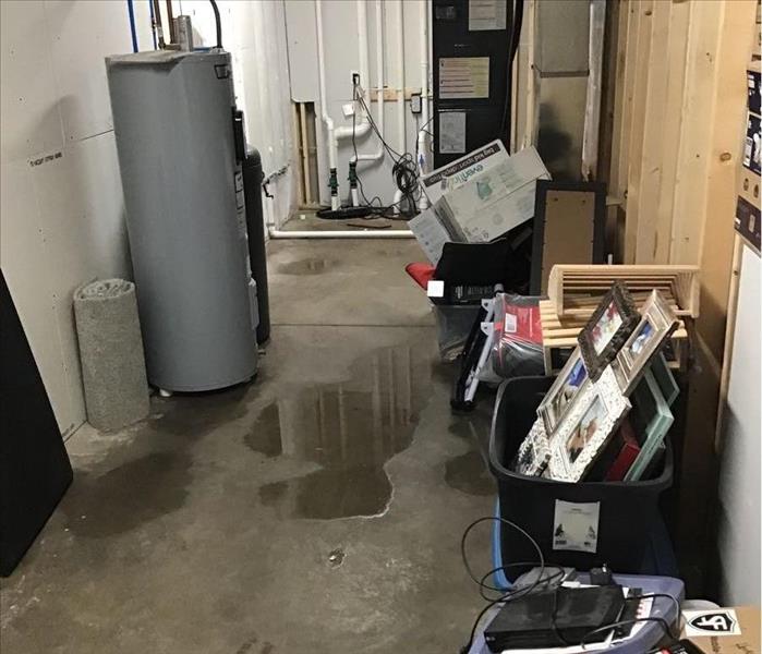 Large utility room in the basement with water on the cement floors.