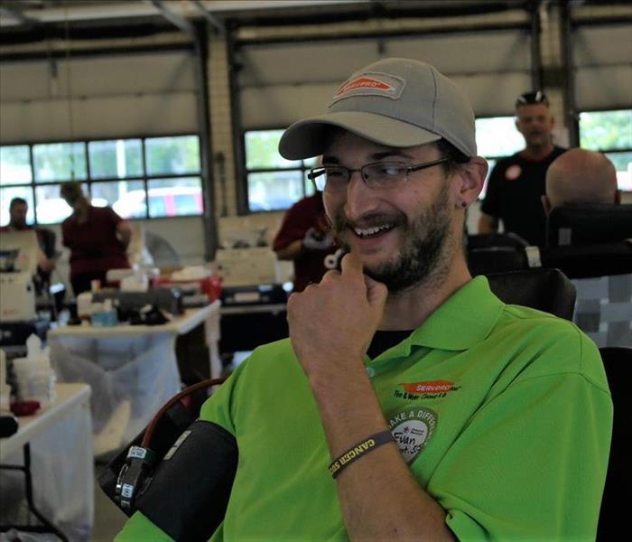 A man with a bright green shirt smiling as he is about to donate blood.