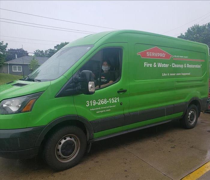 A young woman with black hair and a face mask driving a green transit truck.