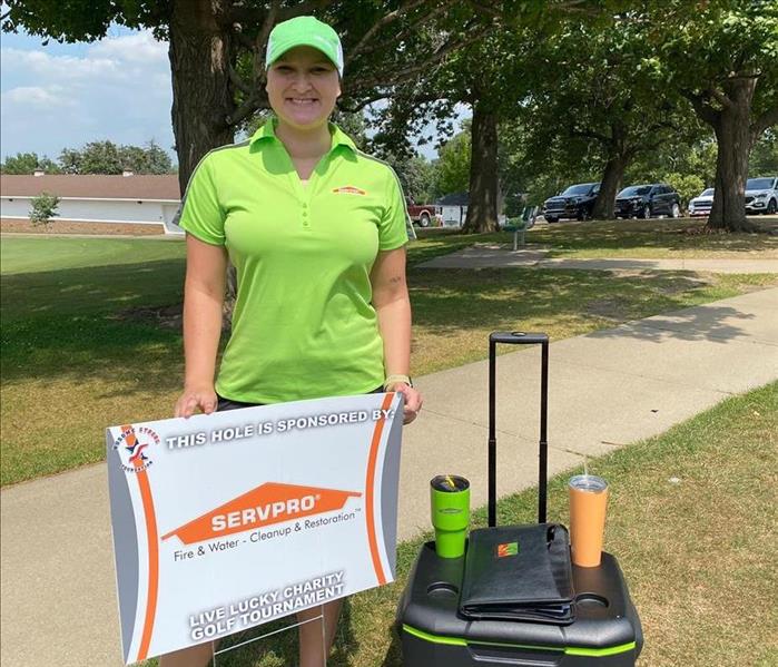 Girl in green shirt behind SERVPRO sign at golf outing