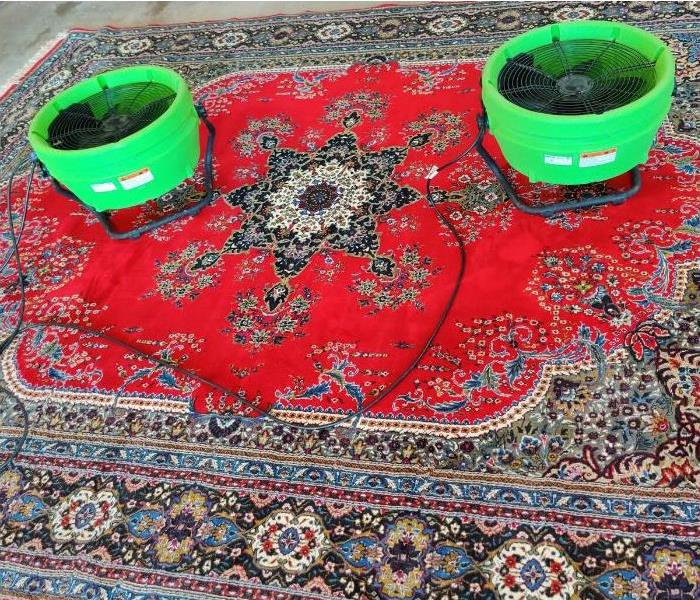 A red oriental rug with two green air movers on it.