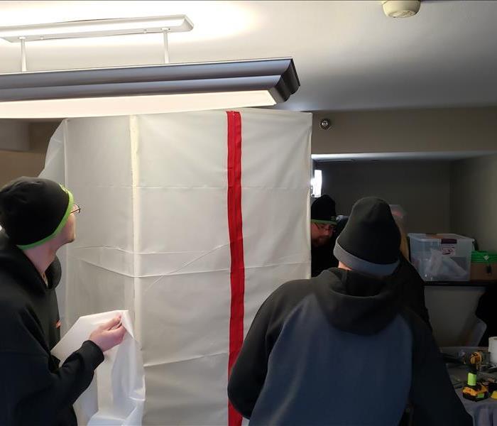 Plastic 7-ft tall chamber with red zipper tape on one side and 3 men gathered around it.
