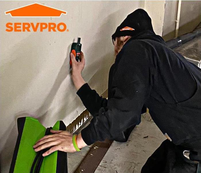 Man in hat doing wet check with hand on equipment + SERVPRO logo 