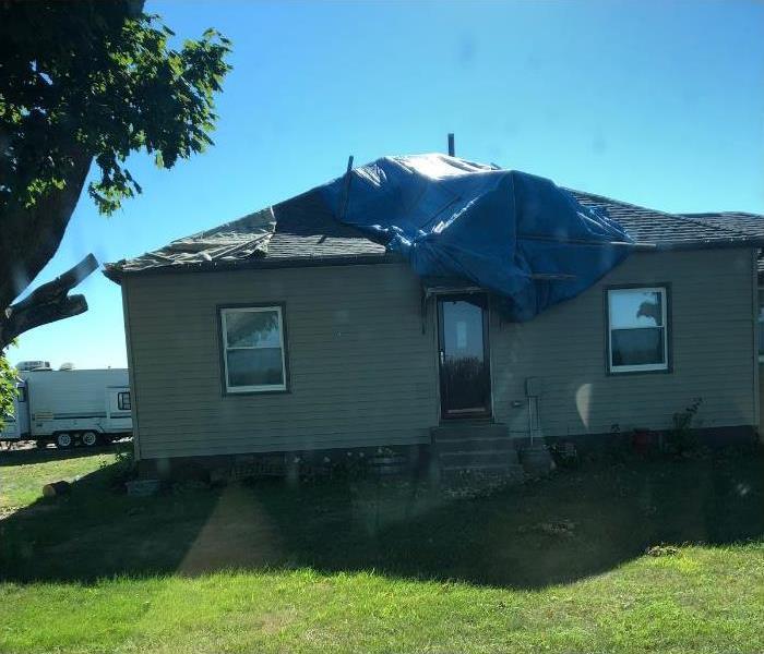 cream colored home with blue tarp over hole in roof