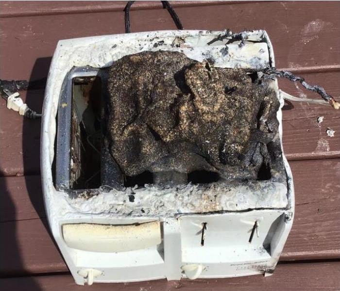 A close up image of a white toaster with burnt marks and a burnt rag on the top part of the toaster.