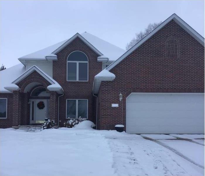 A two story brick home with snow on the roofs and ground.