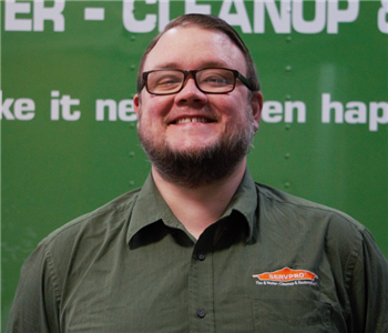 A tall white male with glasses and a baseball cap smiling.